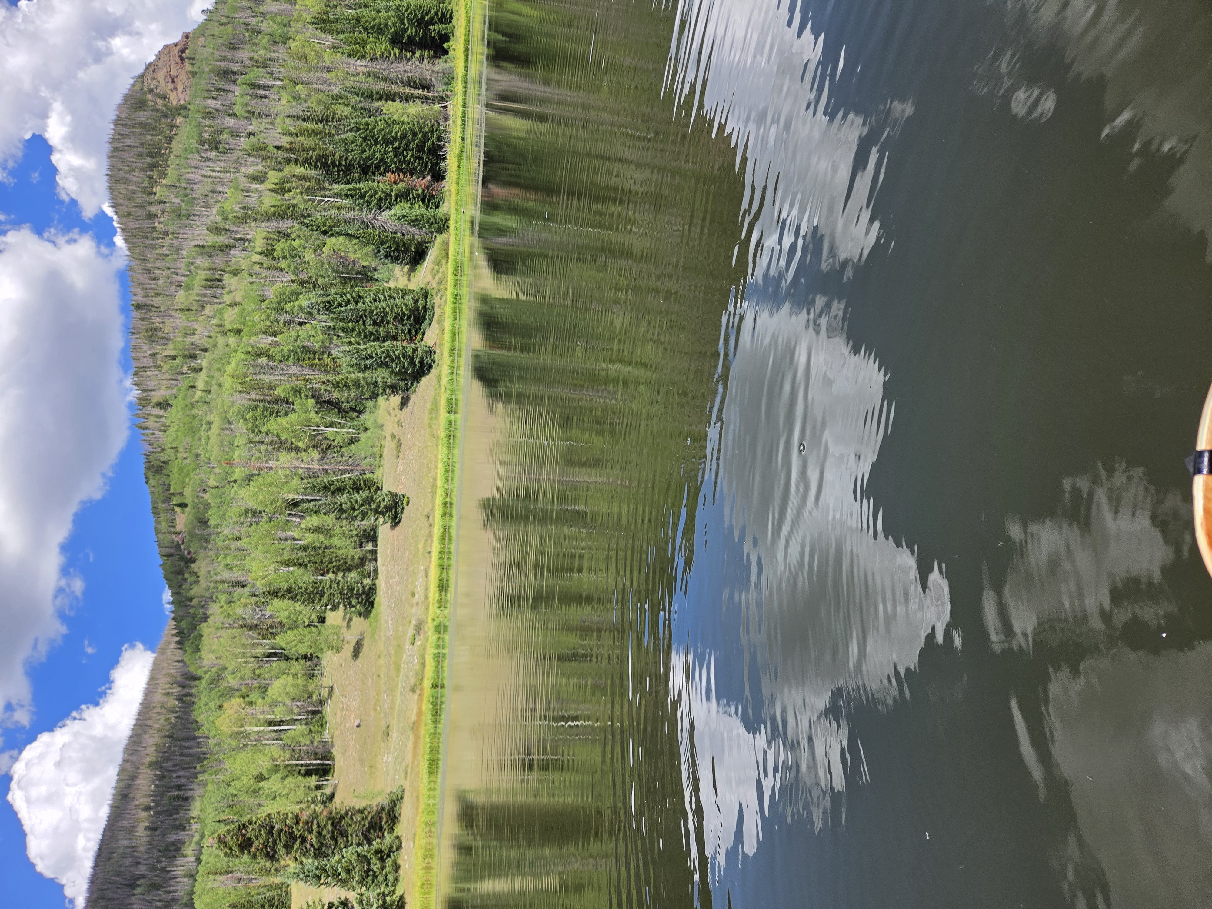 Still mountain lake reflecting clouds and a forested ridge