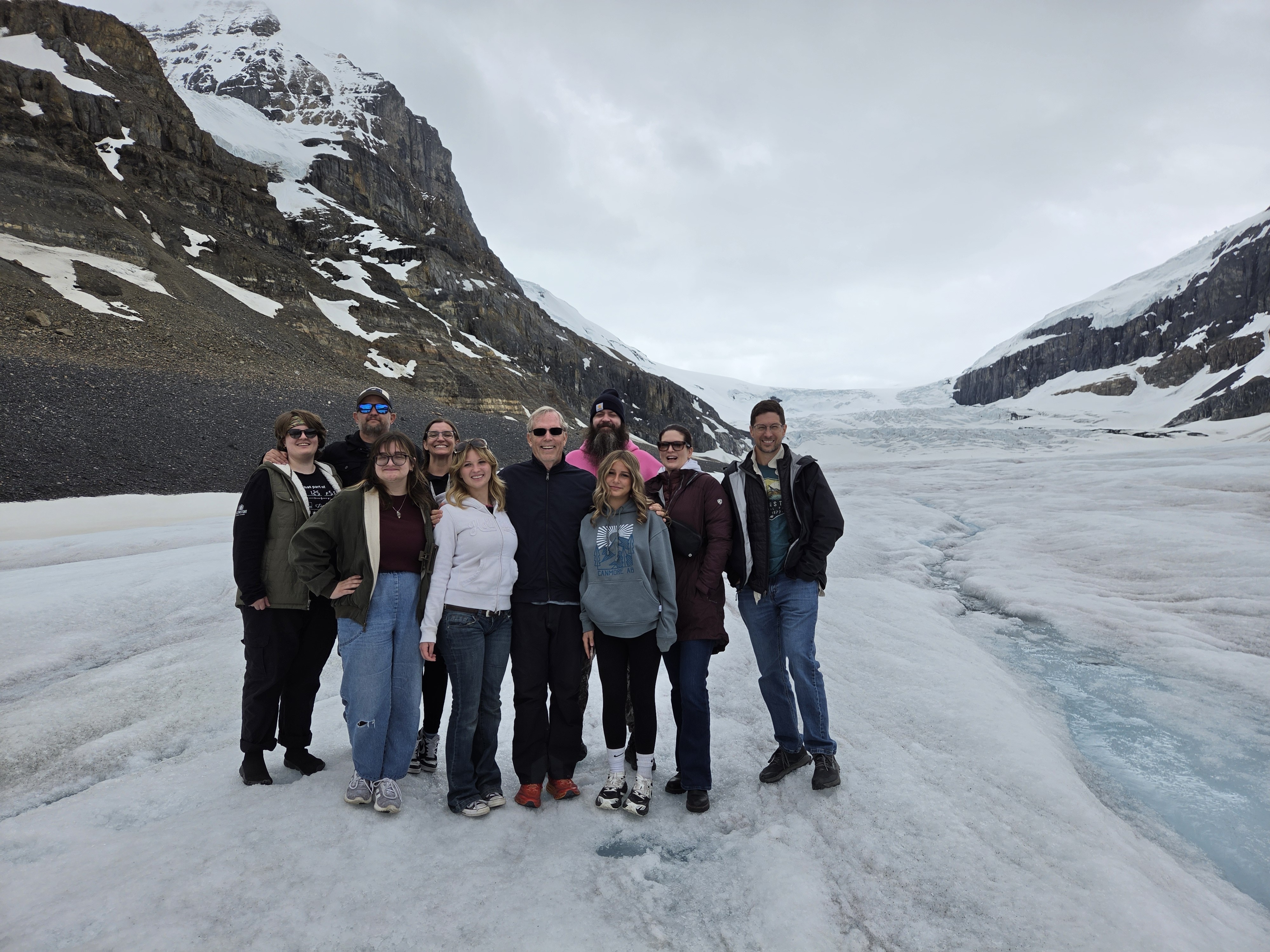 A group standing together out on the open glacier ice, mountains in the distance