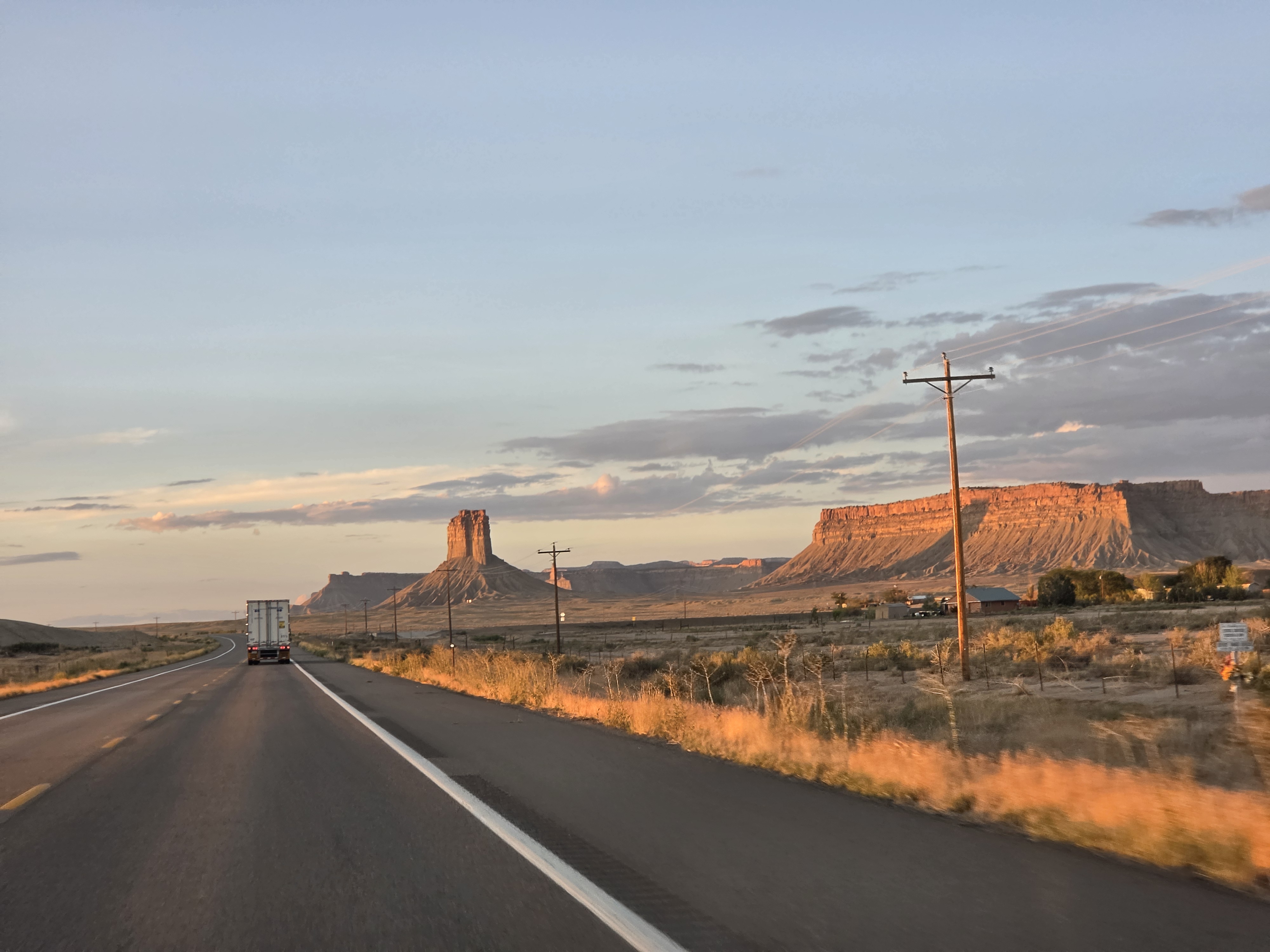 Sunset clouds over buttes along the highway, a semi truck up ahead