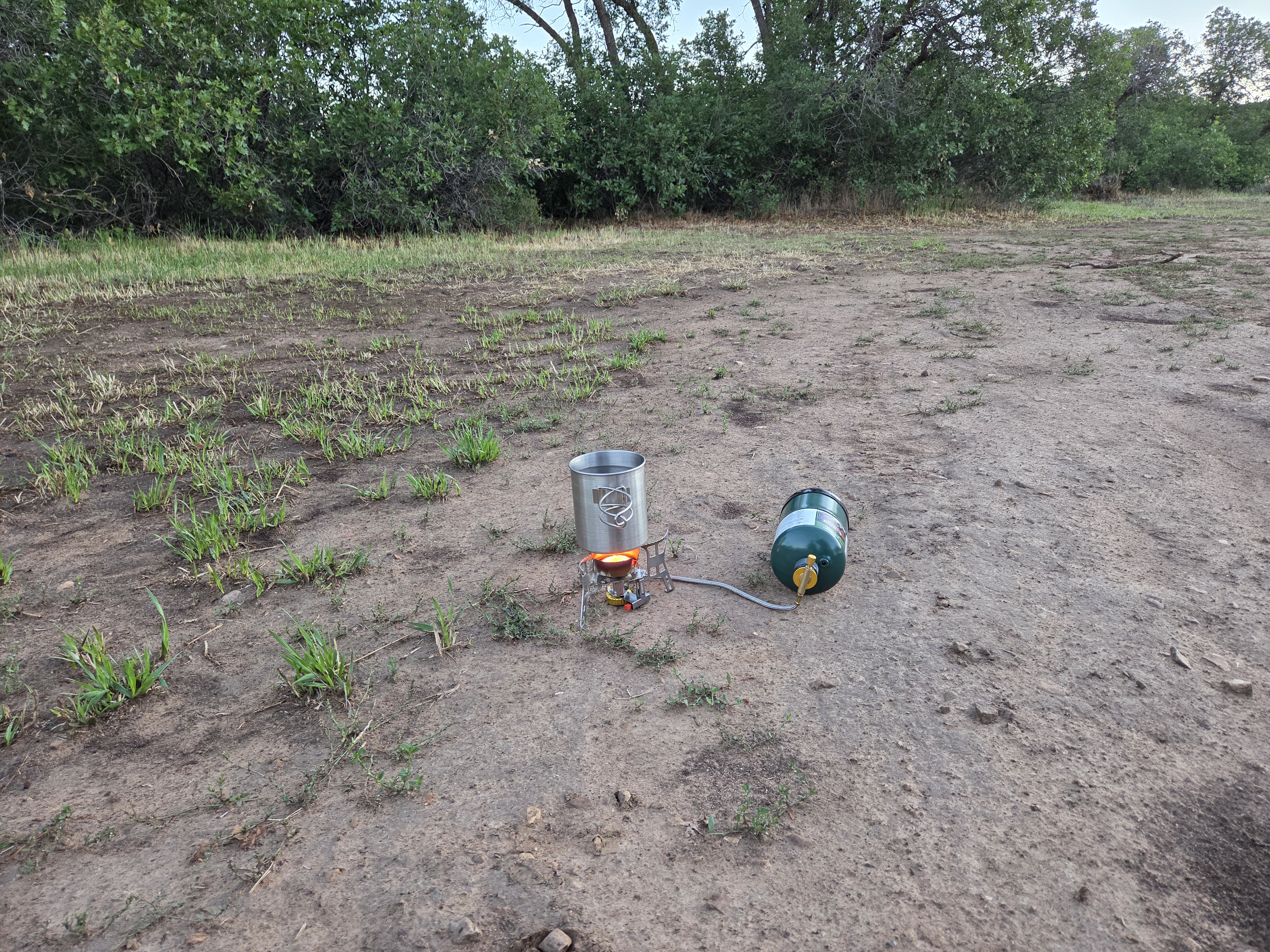 Camp stove and fuel canister set up on the bare ground at camp in the morning