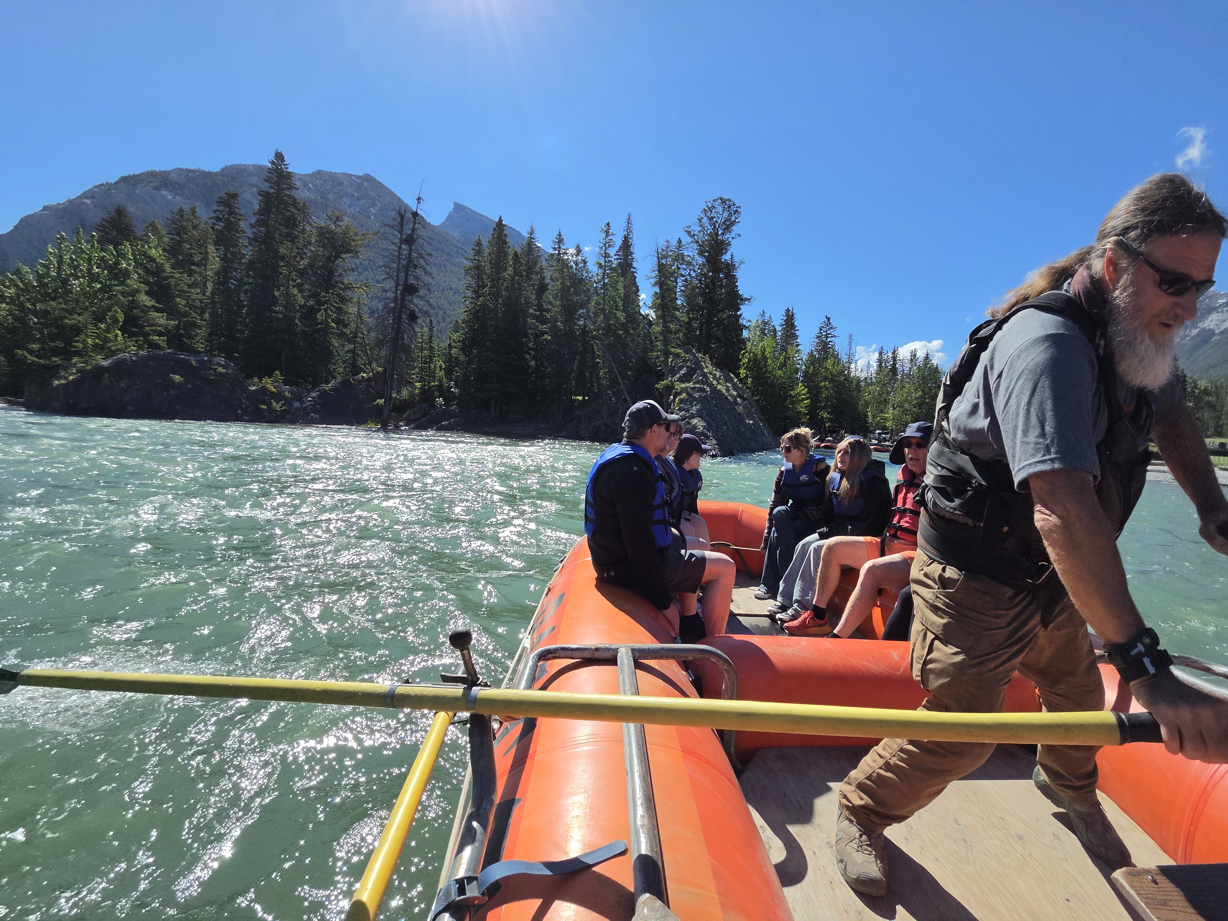 Looking down the raft at the group paddling, everyone in life jackets, the river and far shore ahead