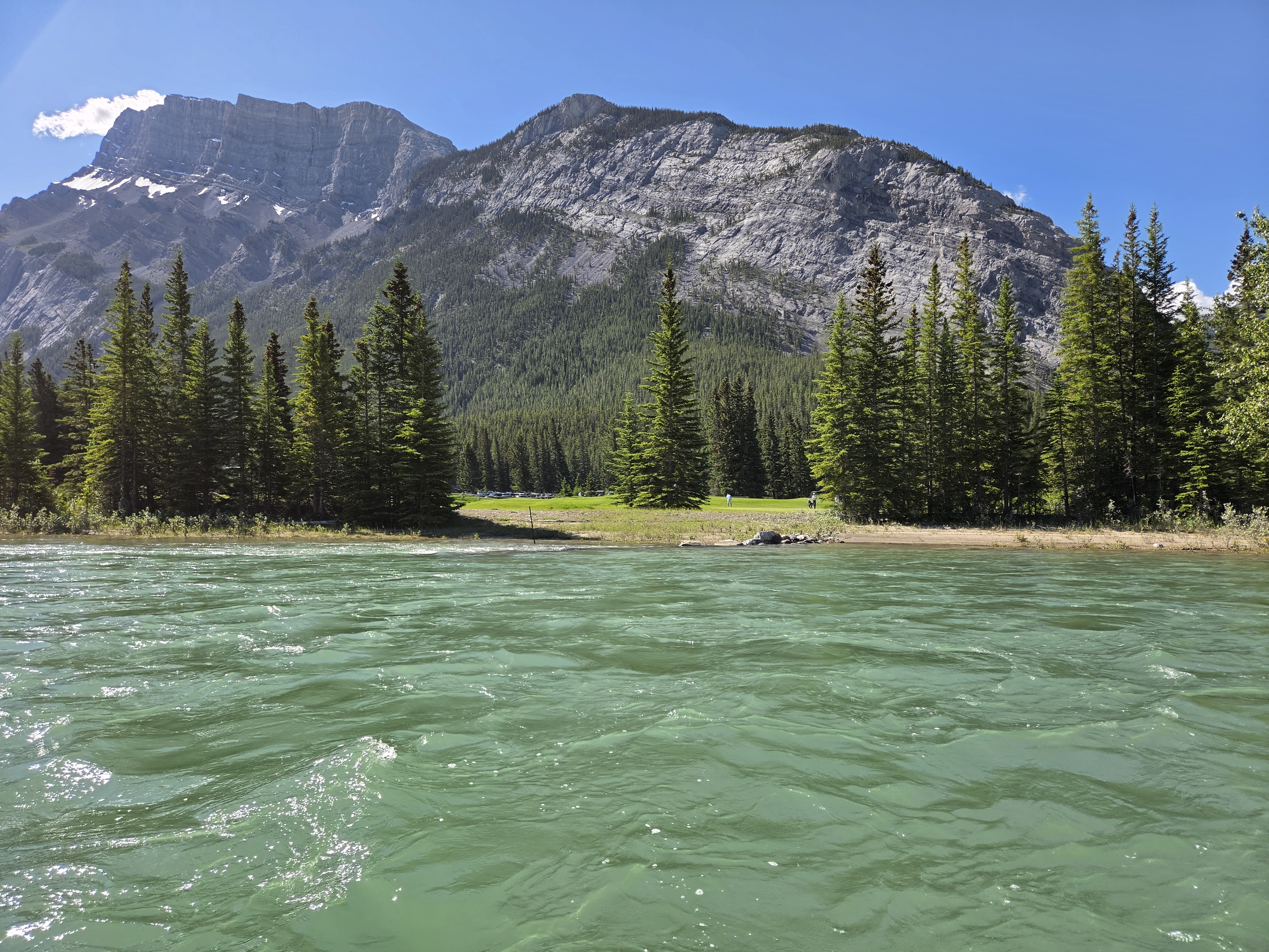 A wide stretch of the Bow River with a forested shoreline and a mountain rising beyond