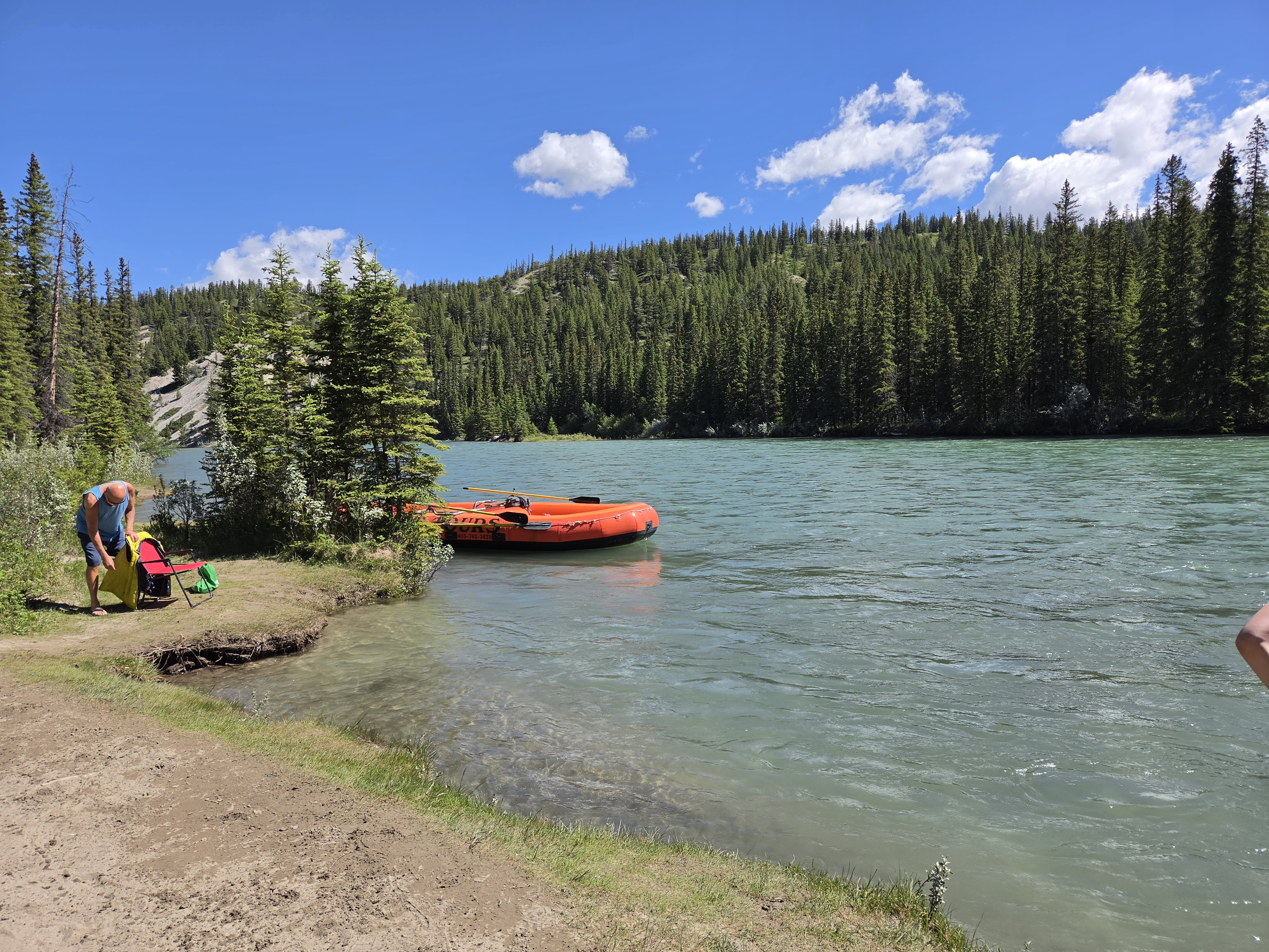 The raft pulled up on a pebbly shore at the take-out, people climbing out, turquoise water and green hillsides behind