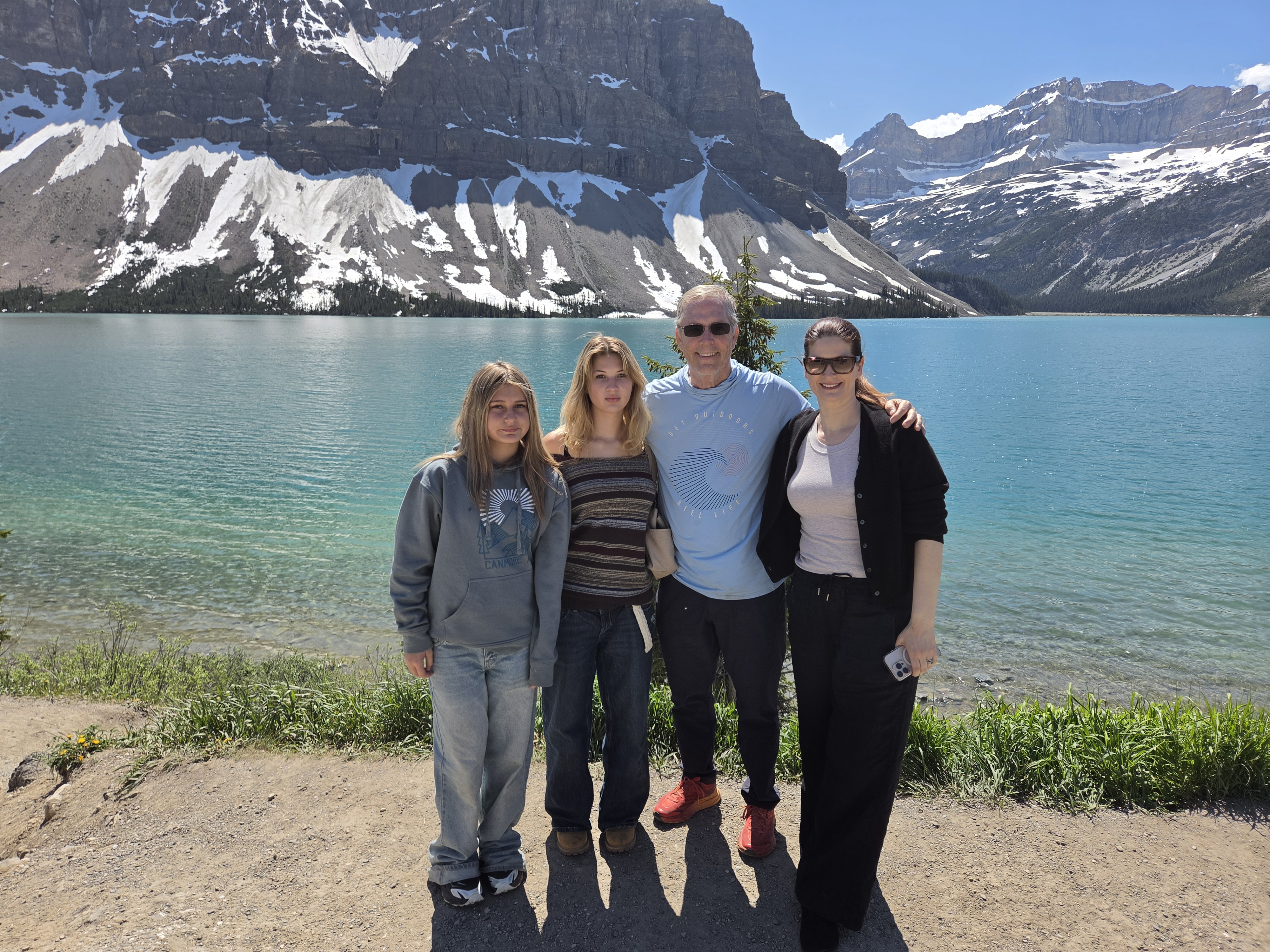 Four people standing together at the shoreline of Bow Lake, mountains rising across the water