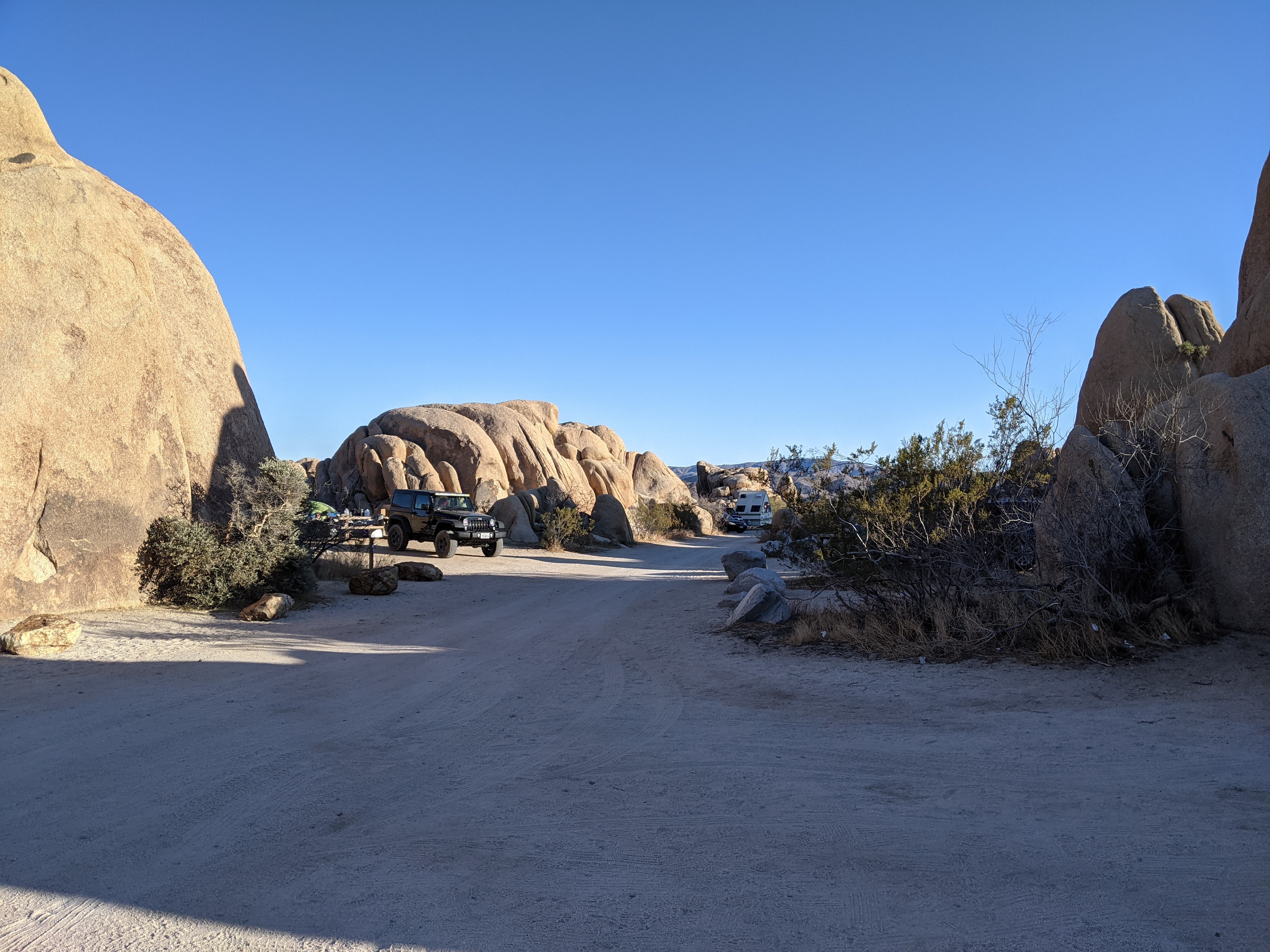 The campground area at golden hour, with a Jeep and RV parked between boulders