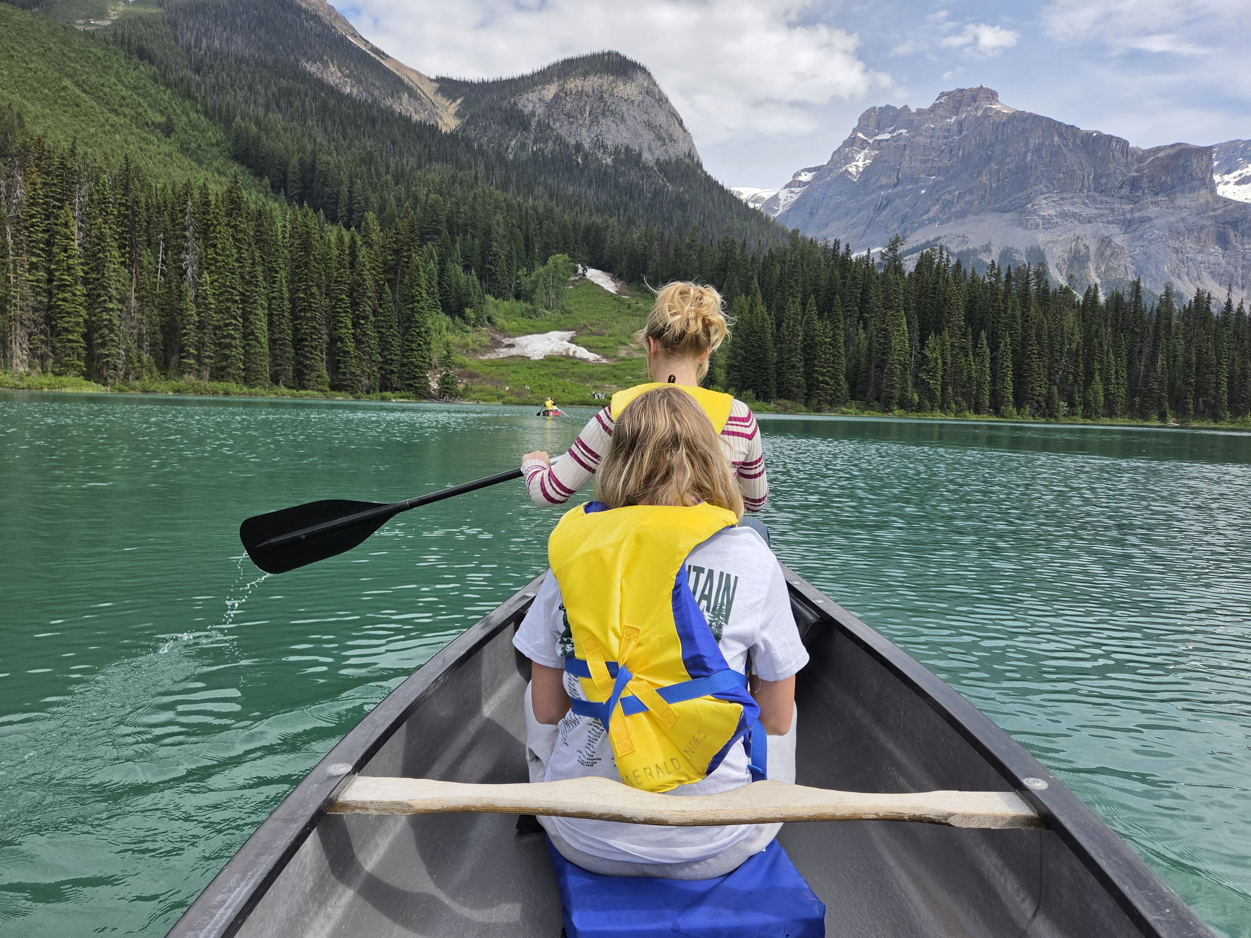 Looking down the length of Emerald Lake from the canoe, calm green water reflecting the forested slopes, a few other canoes far across the lake
