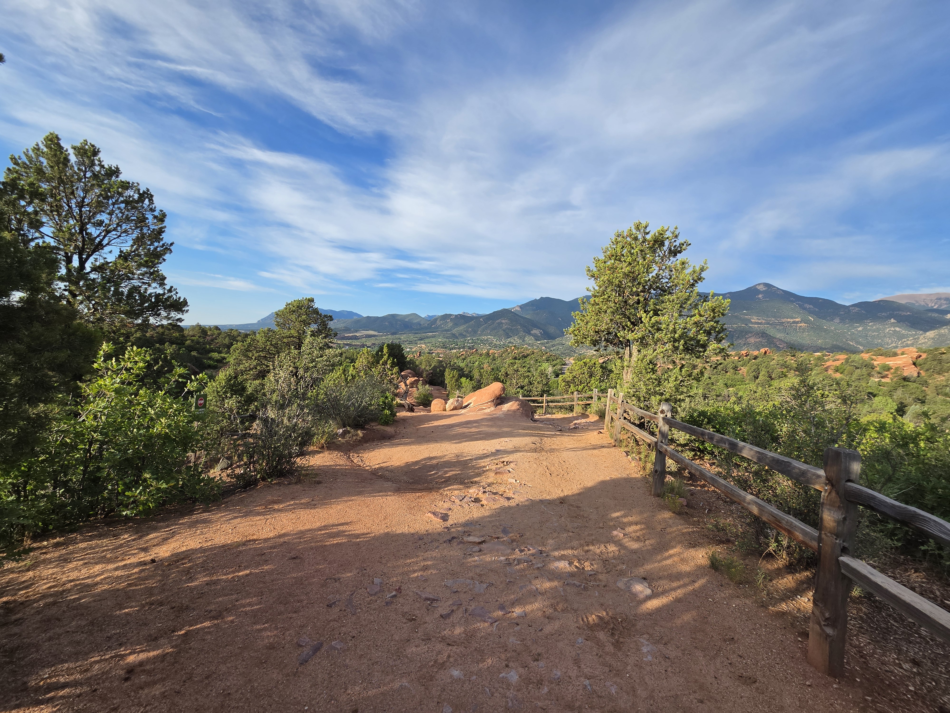 Dirt trail with a wooden fence, mountains in the morning light
