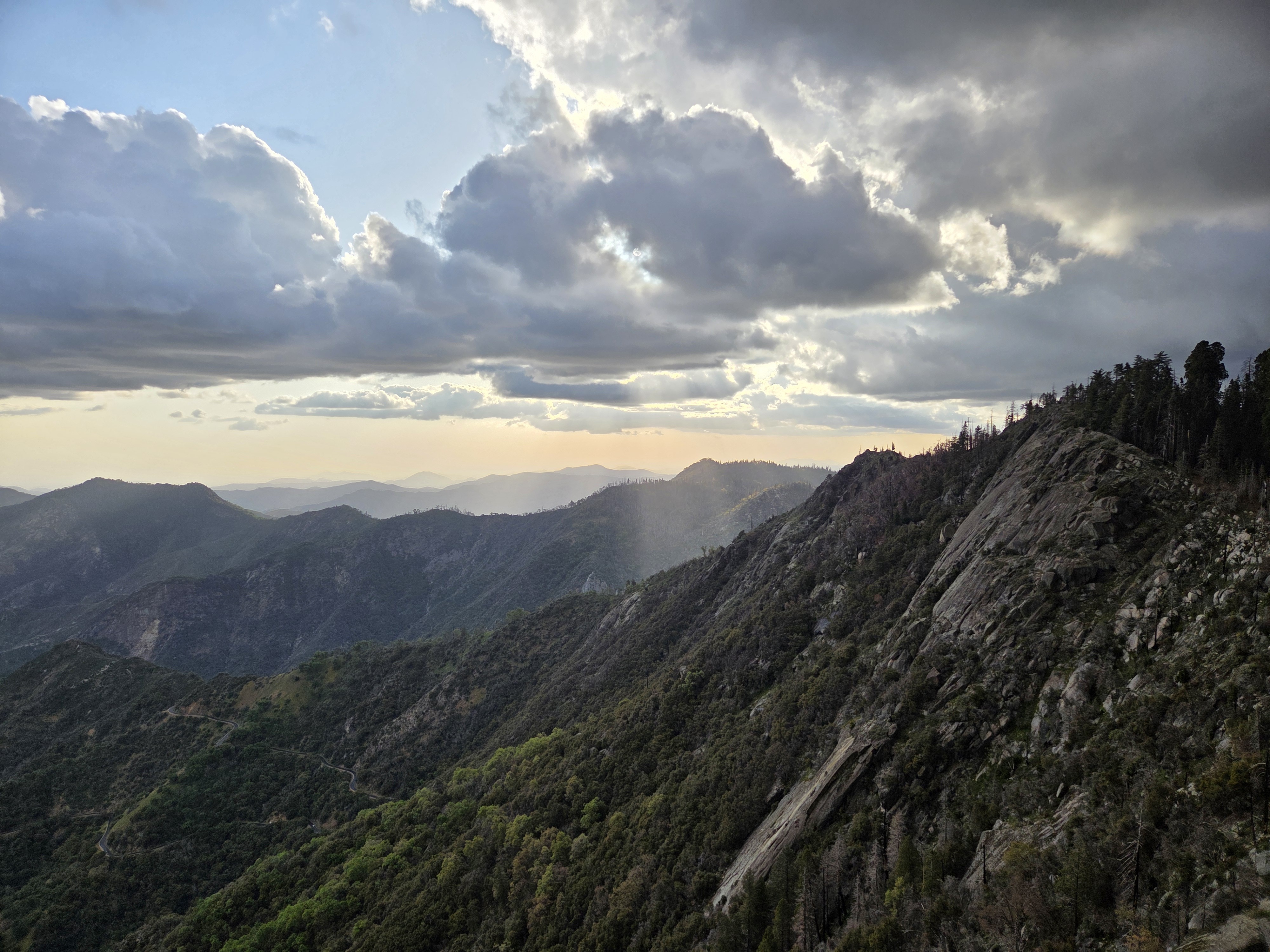Panoramic view of the Sierra Nevada from the Moro Rock area — granite slope on the right, rolling ridges and dramatic clouds beyond