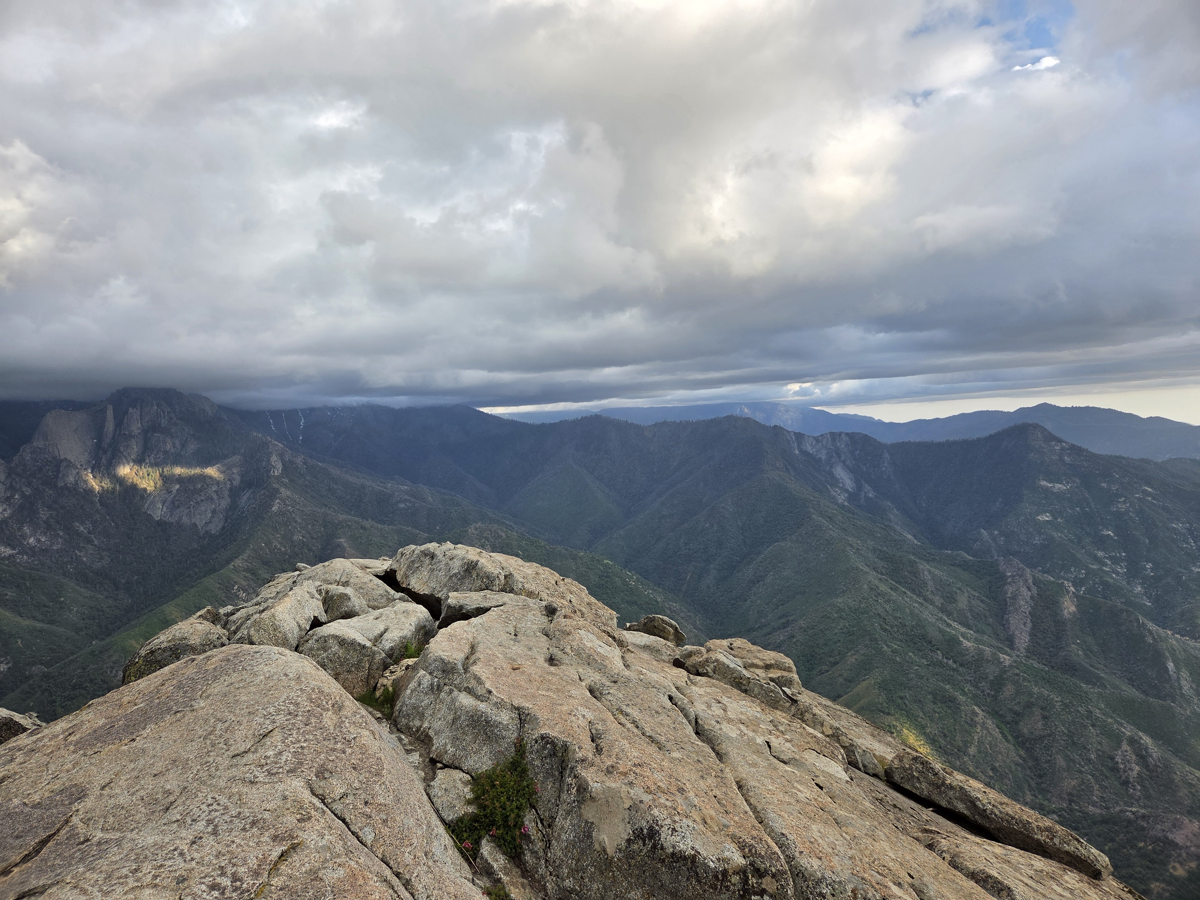 View from the summit of Moro Rock — granite foreground, Sierra Nevada ridges stretching to the horizon, dramatic cloud bank